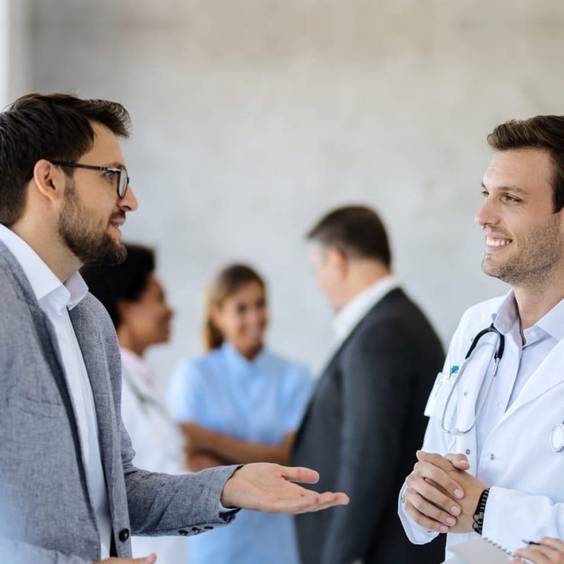 Happy,Healthcare,Workers,Communicating,With,A,Businessman,While,Standing,In